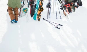 Skis, snowboards et bâtons plantés dans la neige devant un skieur, illustrant le service de location de ski Colette Sport